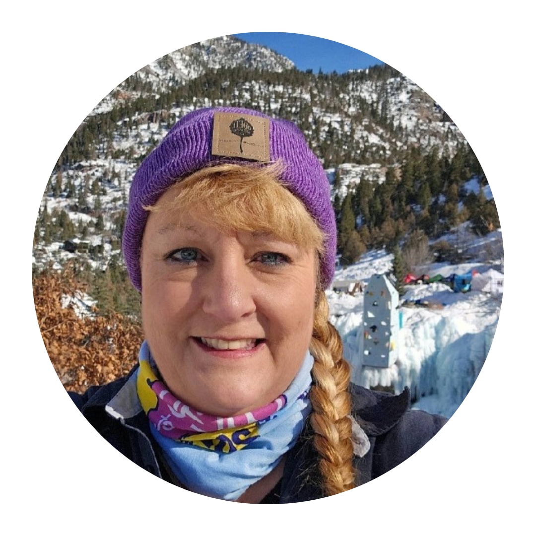 A person in a purple beanie and braided hair is outdoors with snowy mountains in the background.