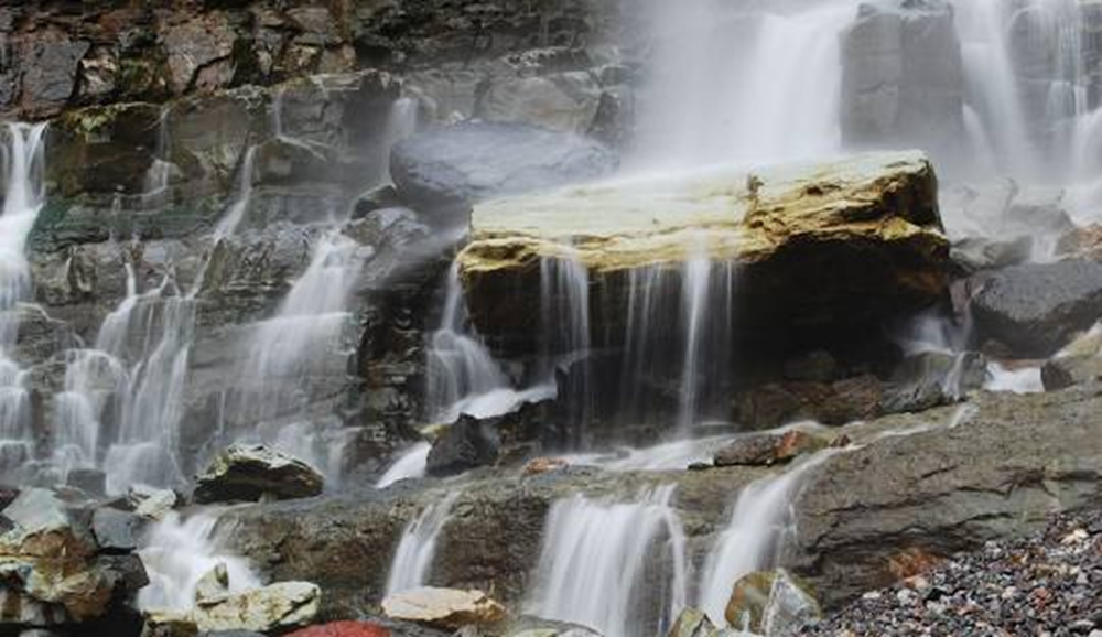 A cascading waterfall flows over jagged rocks, creating mist and small streams below.