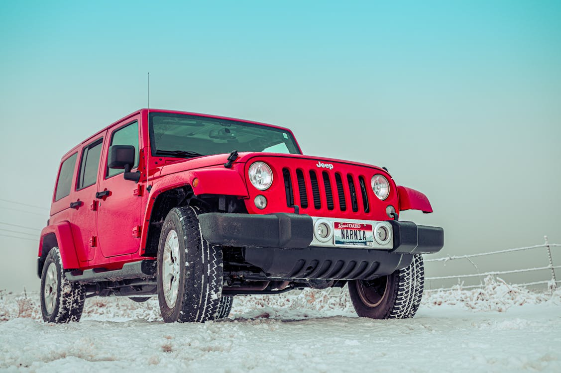 Red Jeep Wrangler parked on a snowy road, with a clear blue sky in the background.