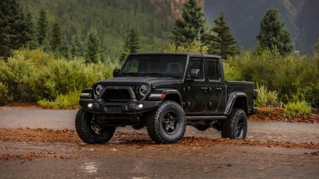 A black pickup truck drives on a muddy path with trees and mountains in the background, showcasing the thrill you could experience with an off-road vehicle rental.